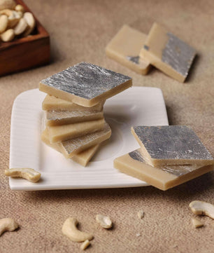 Hand reaching for a piece of Kaju Katli, a popular cashew-based Indian dessert, on a festive table setting.