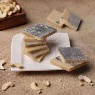 Hand reaching for a piece of Kaju Katli, a popular cashew-based Indian dessert, on a festive table setting.